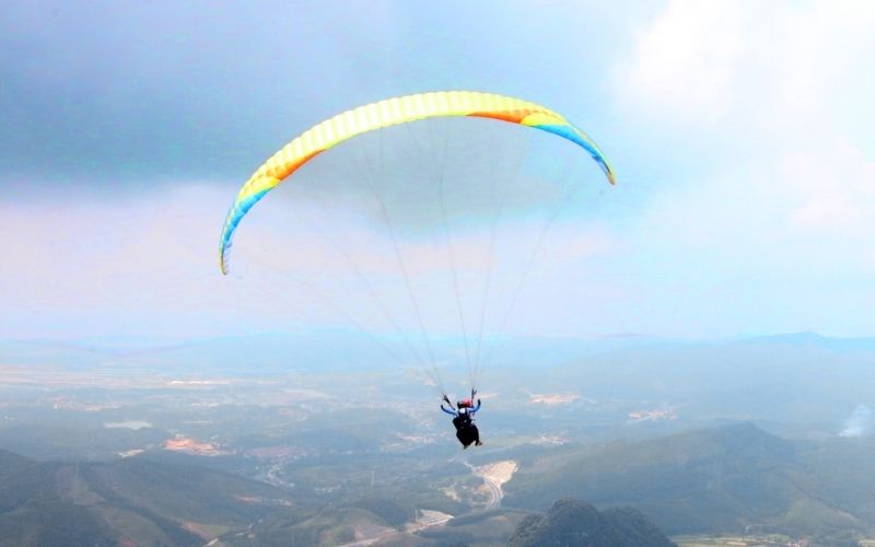 Paragliding over mountainous terrain and cloud-covered valleys in Khao Kho, Thailand.