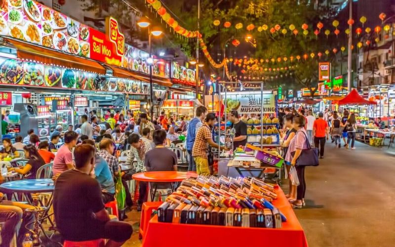 Colorful night view of Kampung Baru Market in Kuala Lumpur, Malaysia, filled with food stalls, vibrant lights, and people enjoying local Malay dishes