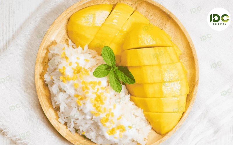 Khao niew mamuang, Thai mango sticky rice with sliced mango and coconut sauce, garnished with mint.