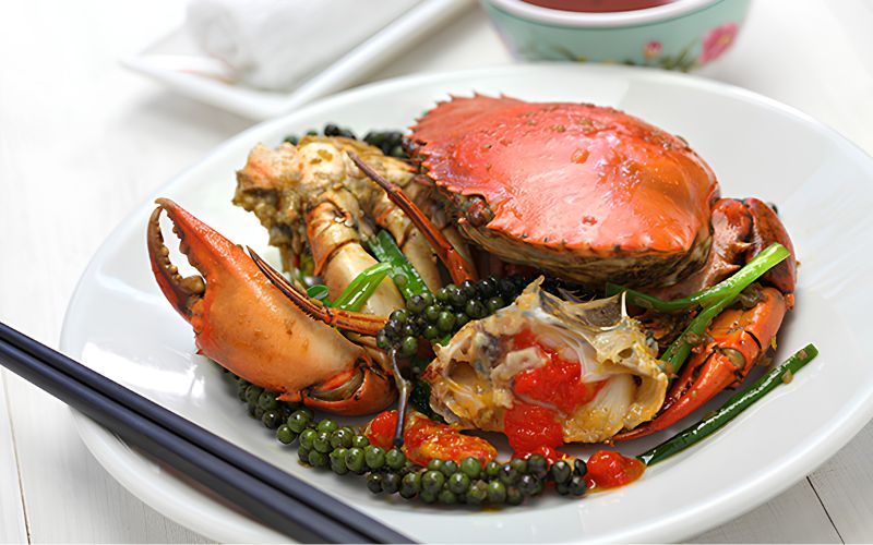 Whole crab stir-fried with fresh Kampot green peppercorns, chili, and spring onions, served on a white plate with chopsticks.