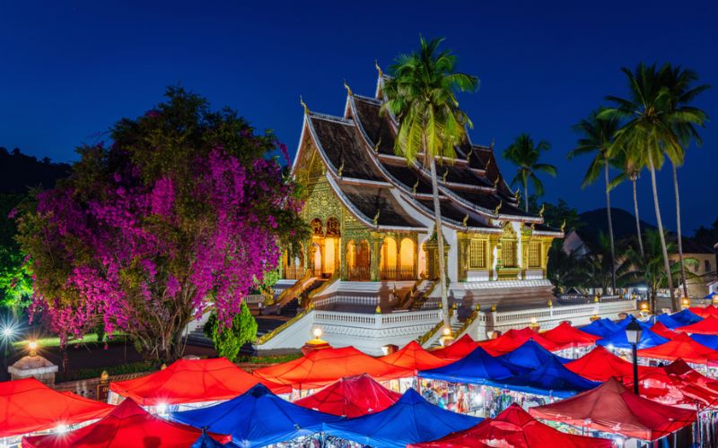 Colorful tents line the Luang Prabang Night Market in Laos, set against a serene temple backdrop, offering handmade crafts and vibrant local goods