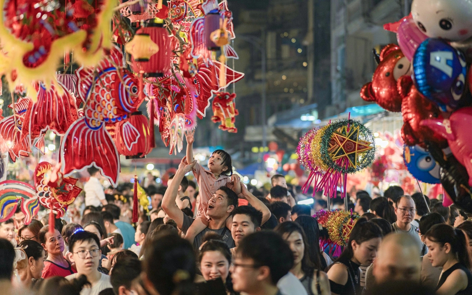 Families and children walking in a lantern parade, holding glowing carp and star lanterns, while singing traditional Mid-autumn songs.