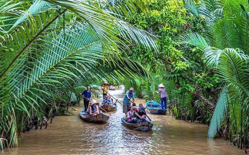 A scenic view of boats gliding through canals surrounded by coconut palms and lush greenery, representing the charm of the new Vinh Long Province after merging with Ben Tre and Tra Vinh.