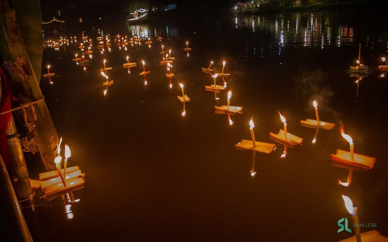 Small wooden Krathongs with candles floating gently on a river during the Loy Krathong Festival in Thailand