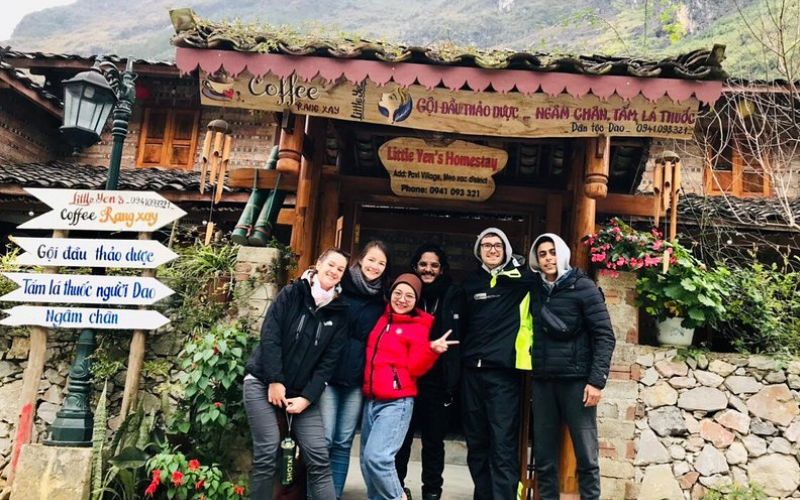 Group of travelers posing in front of Little Yen Homestay, a traditional wooden guesthouse in Meo Vac, Ha Giang, Vietnam