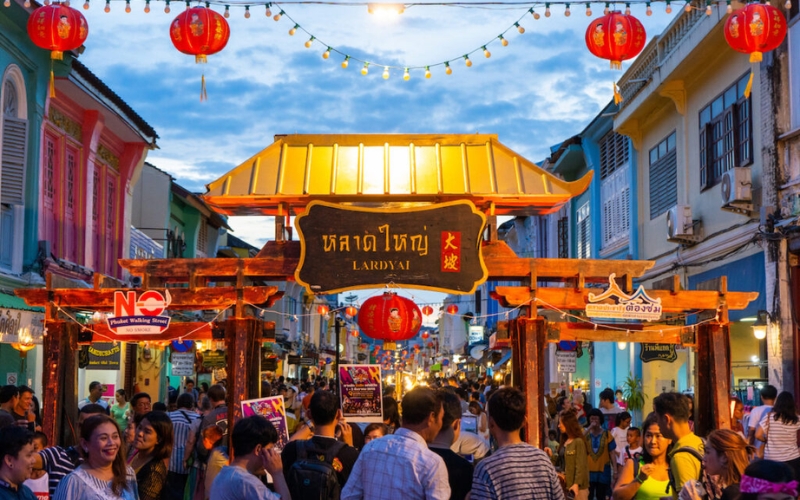 Colorful night market in Phuket filled with food stalls, bright lights, and travelers exploring local street food and handmade souvenirs.