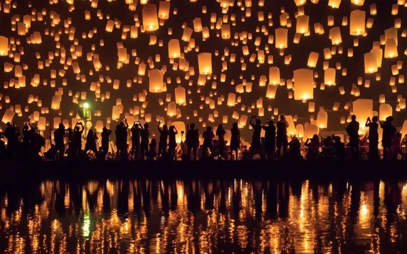 Thousands of glowing lanterns rising into the night sky and reflecting on the water during Yi Peng Festival in Chiang Mai, Thailand