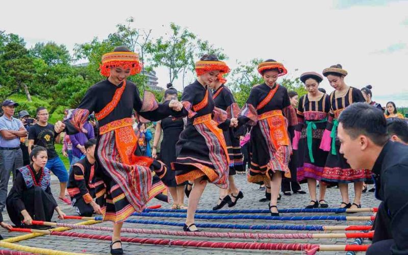 Performers in traditional Thai ethnic attire dancing over bamboo poles during the Mai Chau Festival in Hoa Binh, Vietnam, with a crowd watching