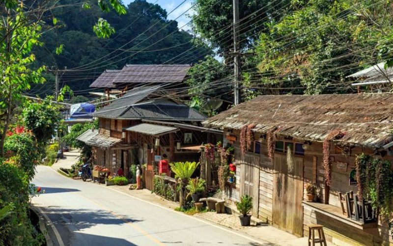 Traditional wooden houses along the road at Baan Mae Kampong village in Chiang Mai, Thailand surrounded by lush green forest.