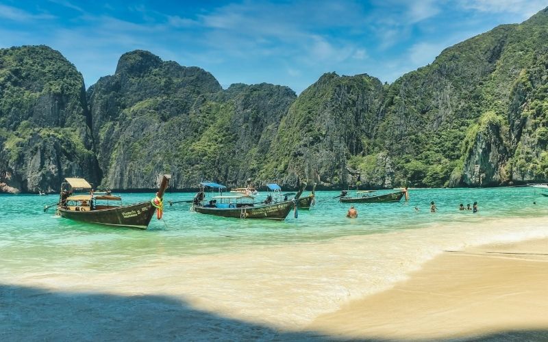 Traditional long-tail boats floating on the turquoise waters of Maya Bay, surrounded by limestone cliffs and lush greenery on Phi Phi Island, Thailand.