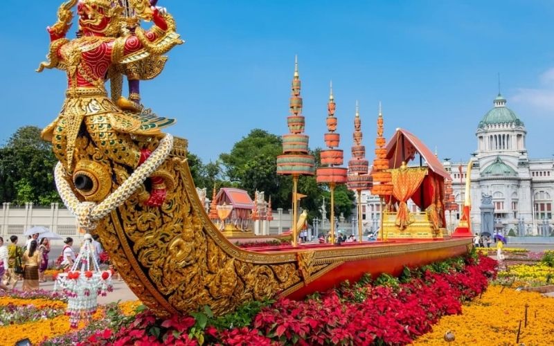 A decorative royal barge float adorned with flowers on display in front of Thai temples and government buildings, celebrating Mother’s Day in Thailand on August 12