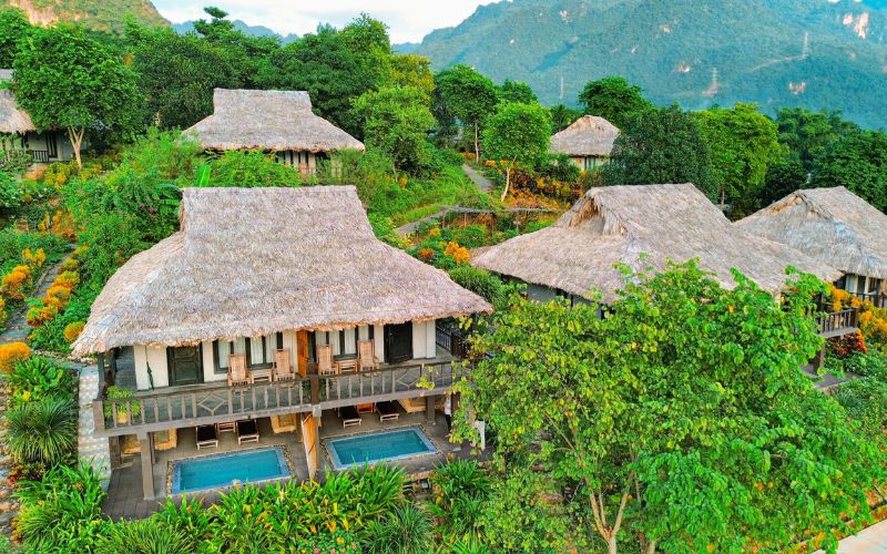 Aerial view of Mai Chau Ecolodge in Hoa Binh, Vietnam, featuring traditional thatched-roof villas surrounded by lush greenery and mountain scenery