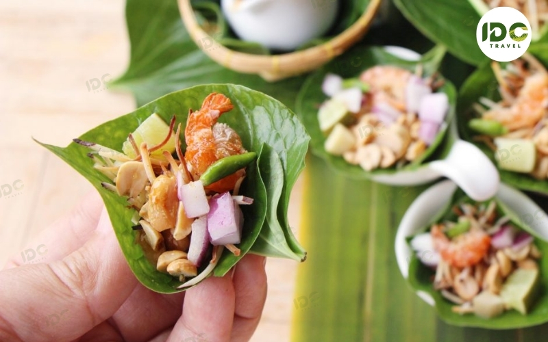 Miang kham, a Thai leaf-wrapped snack with shrimp, peanuts, lime, and diced vegetables, held in hand.