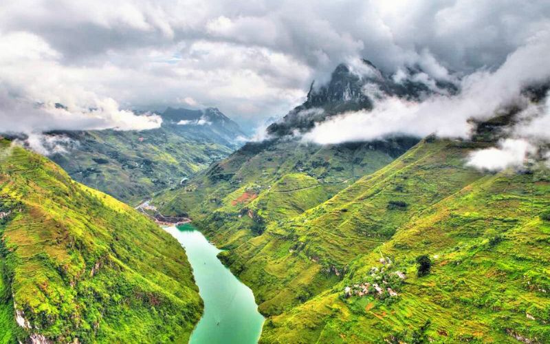 Panoramic view of Ma Pi Leng Pass in Ha Giang, Vietnam, with a winding turquoise river cutting through steep green mountains under a cloudy sky