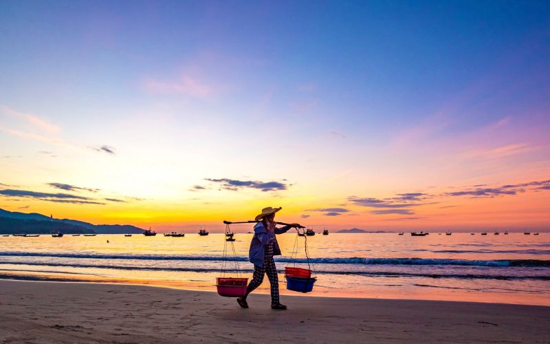 Man Thai fishing village in Da Nang: local fisherman at sunrise, serene beach scene with boats and colorful sky