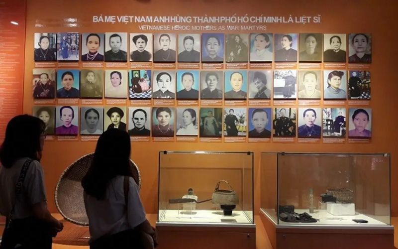 A poignant exhibit inside the Southern Women's Museum featuring a large, bronze-colored statue of a "Heroic Mother of Vietnam." The mother figure is depicted with a serene yet strong expression, wearing traditional clothing. Behind the statue is a commemorative wall with inscriptions honoring the sacrifices made by mothers during the war.