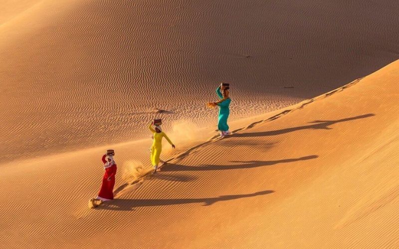 Women in traditional dress walking on golden Nam Cuong Sand Dunes in Ninh Thuan, Vietnam