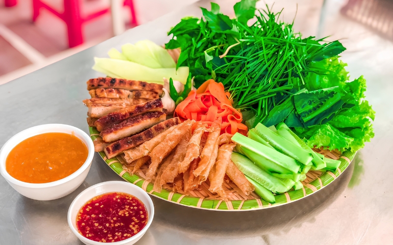 A platter of grilled pork rolls, rice paper, fresh herbs, cucumber, and dipping sauces from Ninh Hoa, Nha Trang.