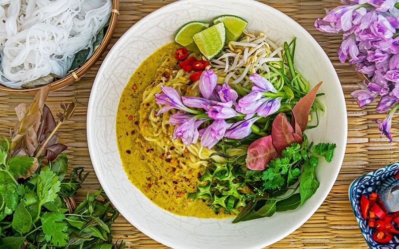 A bowl of Nom Banh Chok, a traditional Cambodian dish with rice noodles, fresh herbs, and colorful garnishes.
