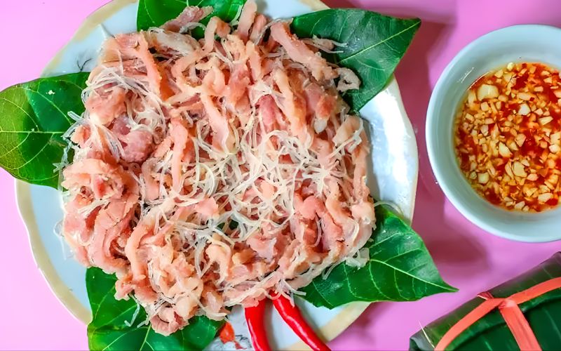 Nem chua Yen Mac, a traditional Vietnamese fermented pork dish, served with chili, garlic sauce, and fresh leaves.