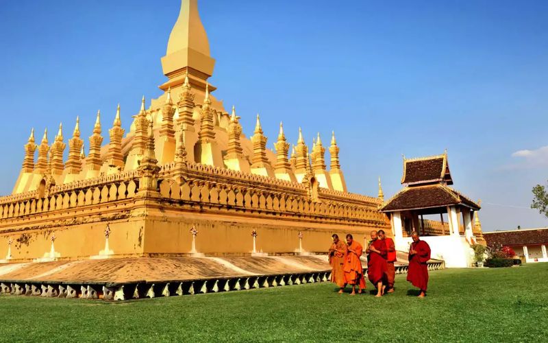 Golden stupa of Pha That Luang in Vientiane, Laos, with Buddhist monks walking nearby.