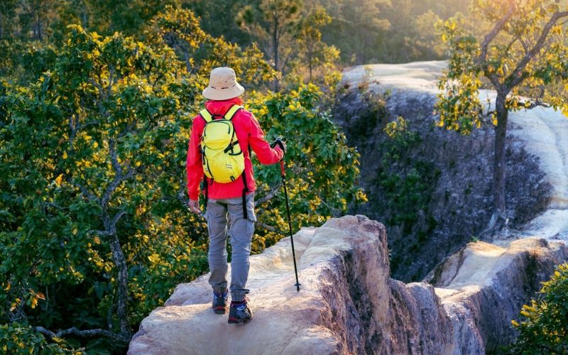 Traveler hiking along the narrow sandstone trail at Pai Canyon in Mae Hong Son, Thailand, surrounded by lush forest during golden hour