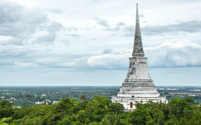 White chedi (stupa) rising above lush greenery, set against a cloudy sky—an iconic landmark in Phetchaburi, Thailand