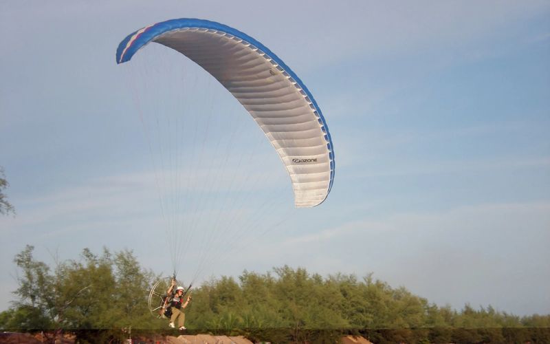 Paraglider descending near coastal greenery in Sihanoukville, Cambodia.
