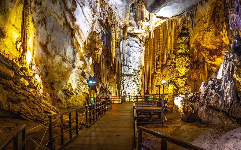 Wooden boardwalk inside Paradise Cave surrounded by massive stalactites and stalagmites lit with warm lighting