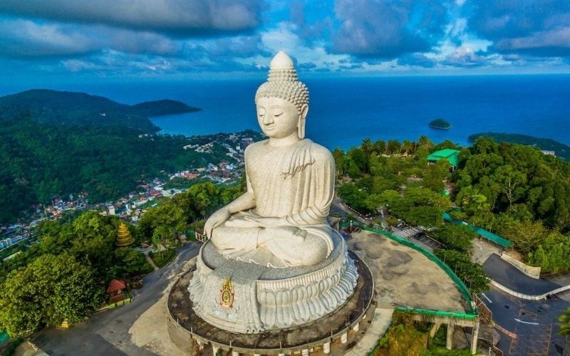 Aerial view of the majestic Big Buddha statue overlooking the lush green hills and coastline near Patong Beach in Phuket, Thailand.
