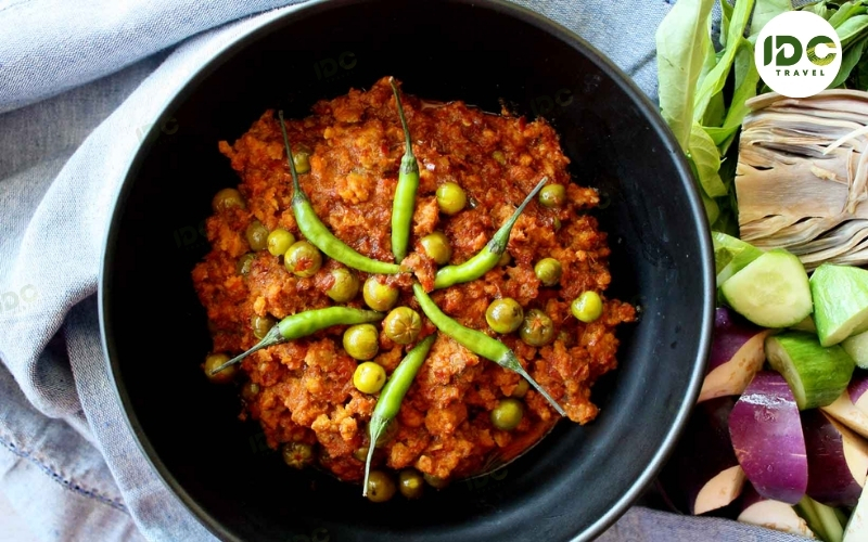 A bowl of prahok ktis, fermented fish and coconut dip topped with green peas and chili, served with fresh vegetables.