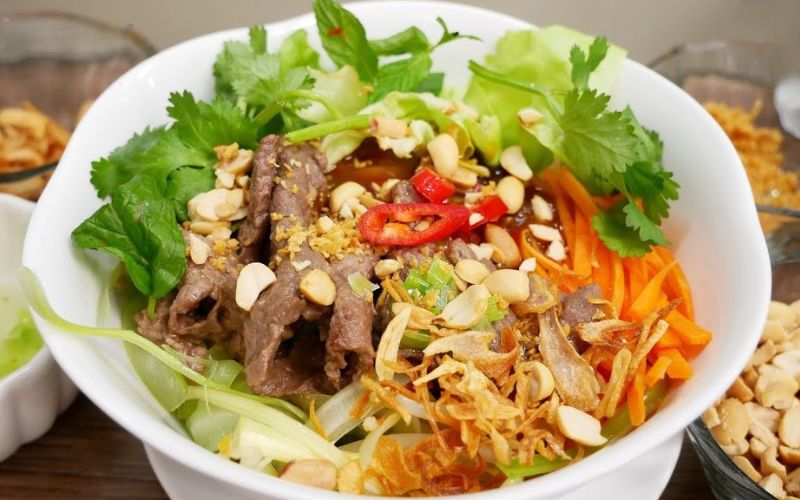 Bowl of pho tron (mixed pho noodles) with beef, herbs, peanuts, and vegetables, served dry with flavorful sauce on the side