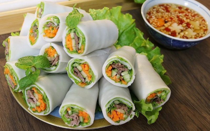 Plate of fresh pho cuon (rolled pho noodles) filled with beef and vegetables, served with lettuce and dipping sauce