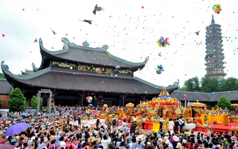 A massive crowd of pilgrims and colorful balloons filling the air in front of a grand temple and stone pagoda during the Perfume Pagoda Festival.