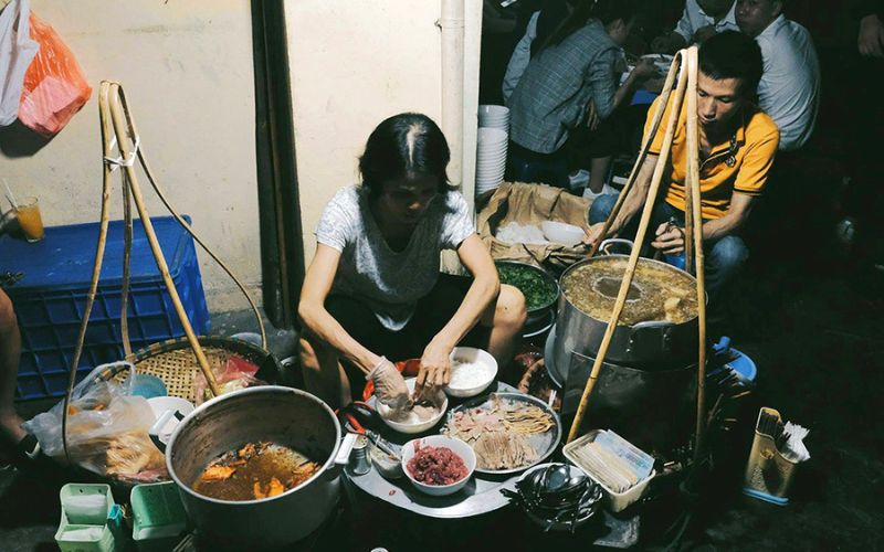 A woman preparing pho at a traditional street vendor stall in Vietnam, showcasing the charm of pho gánh culture