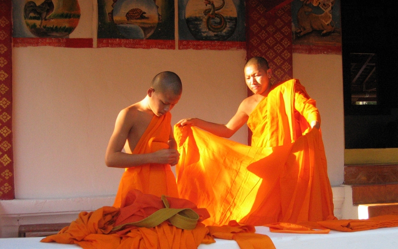 A young man is guided by a monk as he learns to properly wear the saffron robe during his ordination. In Laos and Thailand, it’s common for young males to temporarily enter monkhood at the start of Khao Phan Sa, dedicating this spiritual retreat to self-reflection and merit-making for their families.