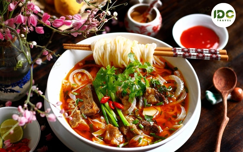 A bowl of pho bo sot vang, Vietnamese beef stew noodle soup with rice noodles, herbs, and red broth.