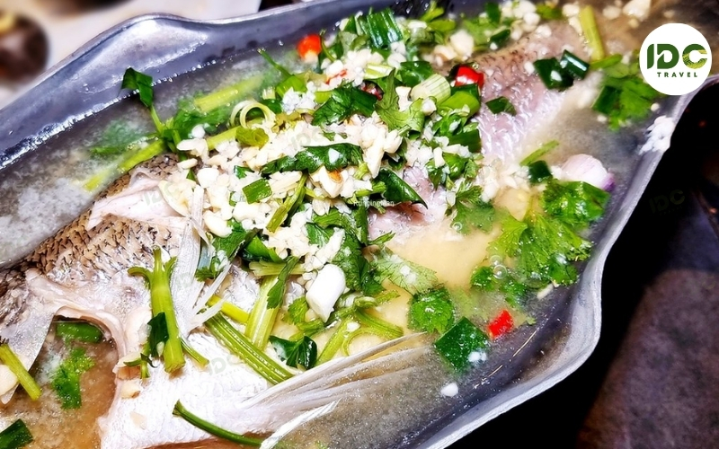 Pla kapong nueng manao, Thai steamed sea bass with lime, chili, and garlic sauce, served on a metal platter.