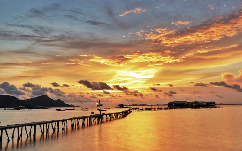 Fiery orange and pink sky reflecting on the calm waters of Phu Quoc, with fishing boats silhouetted against the horizon.