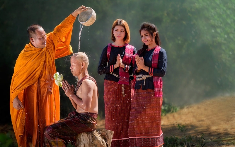 A traditional monk ordination ceremony taking place, with families watching and offering support.