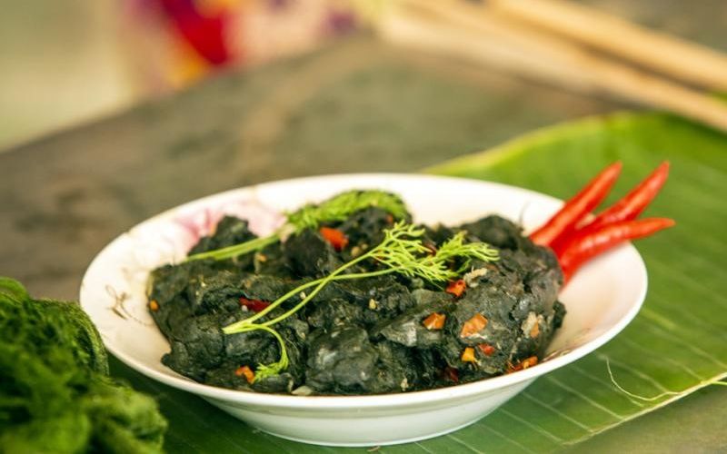 Plate of Vietnamese grilled moss (Reu Da Nuong) garnished with fresh herbs and red chili, served on a banana leaf