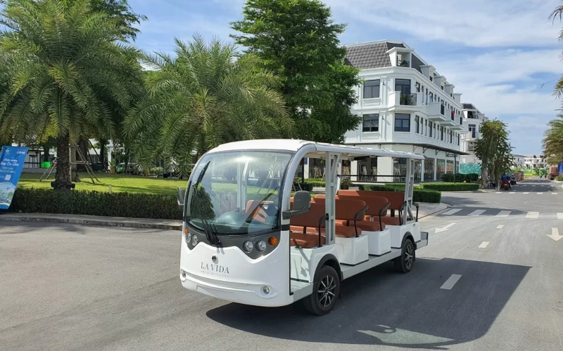 White electric shuttle cart driving through a resort area with palm trees and modern buildings in Nha Trang, Vietnam.