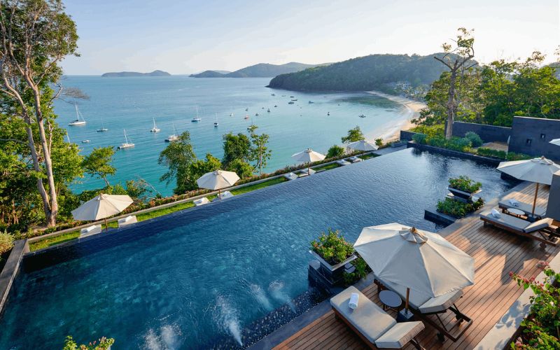 Luxury resort in Phuket with an infinity pool overlooking the sea, surrounded by tropical hills and anchored boats