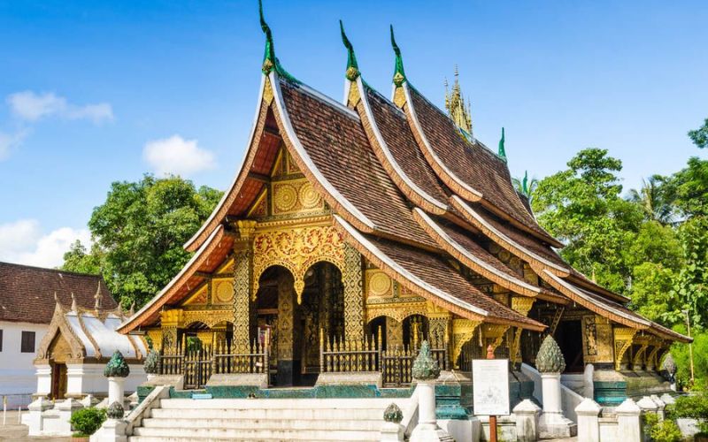 Exterior view of the Royal Palace Museum in Luang Prabang, Laos, showcasing traditional Lao architecture with intricate details and lush greenery surrounding the building.