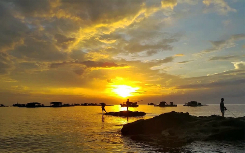 Rocky coastline of Ganh Dau Cape in northern Phu Quoc, with waves crashing against the shore and a golden sunset in the distance.