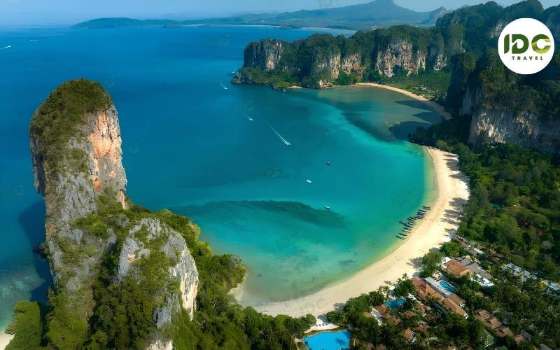 Aerial view of Railay West beach in Krabi, Thailand, with towering limestone cliffs rising from turquoise water.