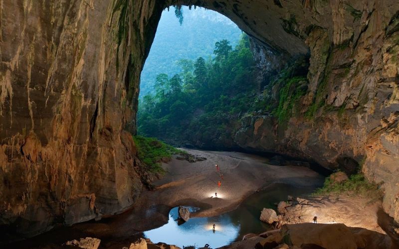Vast chamber inside Son Doong Cave with explorers standing beneath towering limestone walls and natural light entering from above