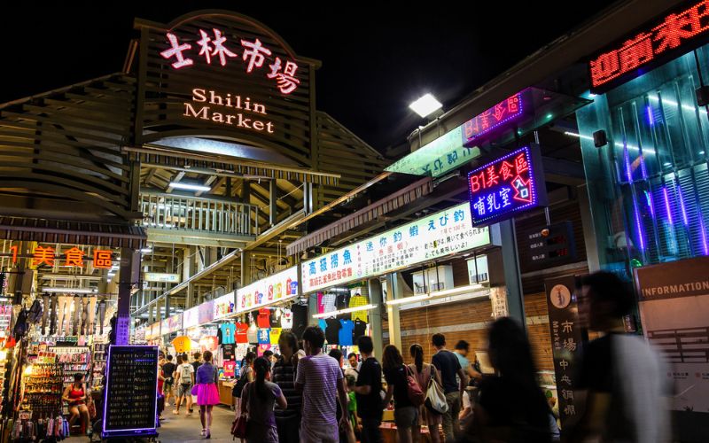 Night view of Shilin Night Market in Taipei, Taiwan, with colorful lights, food stalls, and crowds enjoying local street food