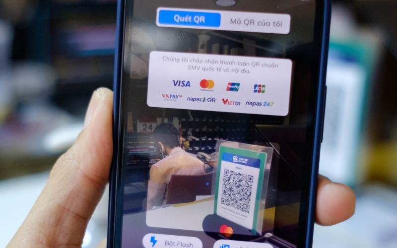 Person scanning a QR code payment sign on a smartphone showing accepted cards and QR payment options in Vietnam.