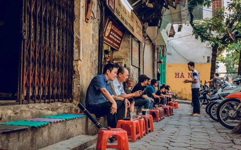 Locals sitting on plastic stools at a sidewalk café in Hanoi, enjoying coffee and conversation in a typical Old Quarter street setting